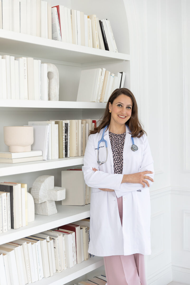 Dr. Farah Siam in white coat by bookshelf